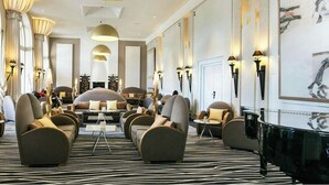 A spacious lounge area with sofas and armchairs, a central table, and wall-mounted lamps. - Impérial Palace (Annecy)