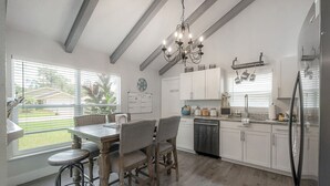 A modern kitchen with a dining area, wooden flooring, and a chandelier.