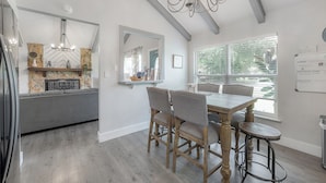 A modern kitchen with a dining area, featuring a chandelier, stone backsplash, and a large window with blinds.