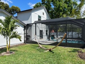 Uma casa moderna com uma grande estrutura de vidro, uma rede e uma pequena palmeira.