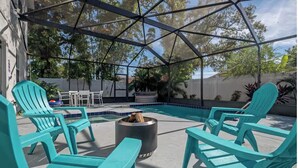 A pool area with turquoise chairs, a fire pit, and a covered patio.