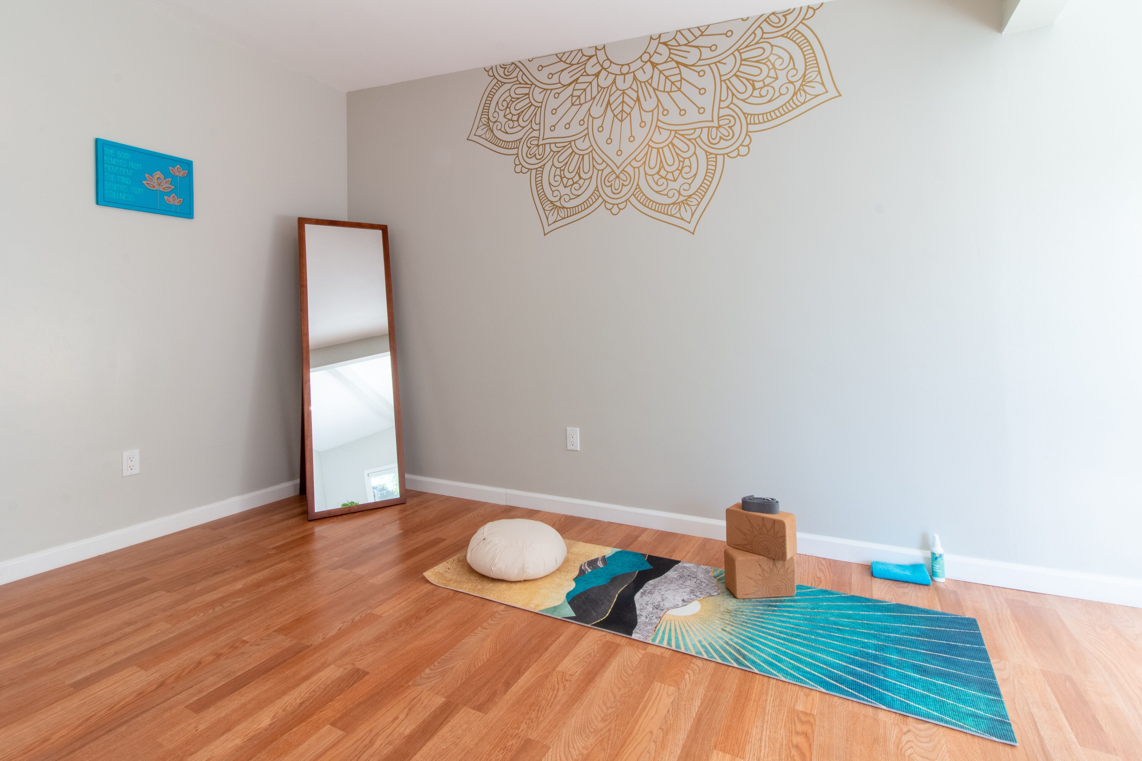 Una sala de ioga amb sòl de fusta, un gran mirall, un matalàs per a la meditació i una paret amb un disseny de mandala.