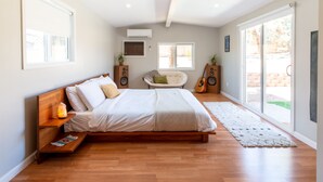 Une chambre à coucher avec un lit en bois, une grande fenêtre, une chaise et une guitare.