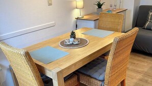 A dining area with a wooden table, wicker chairs, a lamp, and a framed beach picture on the wall.