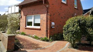 A red brick house with a tiled roof, a front window with shutters, and a small garden with a pathway leading to the entrance.