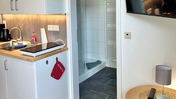 A compact kitchen with a built-in stove, a small sink, and a red towel hanging on the door.