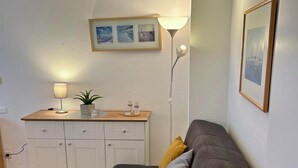 A compact living space with a sofa, a small table with a lamp, a cabinet, and a framed picture on the wall.