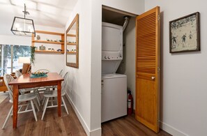 Een kamer met een eettafel, stoelen, een witte wasmachine en een houten deur.
