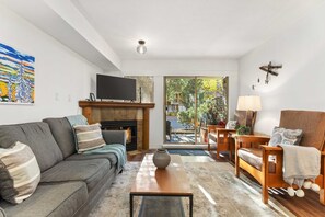 Un salon comprenant un canapé, une table basse, une cheminée, un téléviseur et une vue sur l’extérieur.