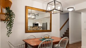 Un comedor con una mesa de madera, cuatro sillas, un espejo grande y una planta colgante.