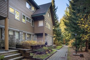 Un immeuble résidentiel à plusieurs étages, agrémenté d’éléments en pierre, doté d’un jardin aménagé avec des marches menant à l’entrée, et d’un chemin bordé d’arbres.