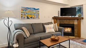 Una sala de estar con un sofá gris, una chimenea, un televisor y un cuadro en la pared.