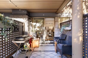 Un espace extérieur abrité, équipé d’un barbecue, de plantes en pot et d’un coin salon avec un fauteuil en osier.