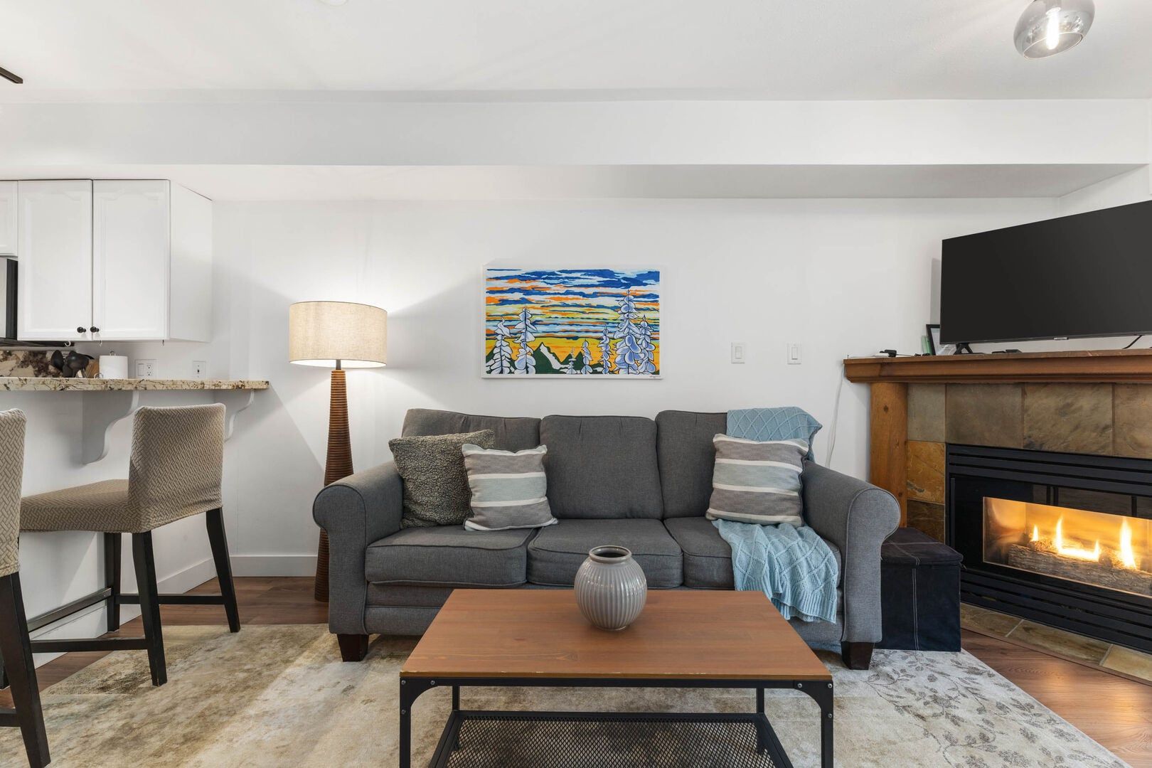 Een woonkamer met een bank, salontafel, open haard, televisie en een schilderij aan de muur.