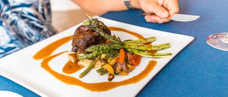 A beautifully plated gourmet meal awaits you at the property's restaurant, featuring succulent meat, fresh grilled vegetables, and an artful sauce presentation.