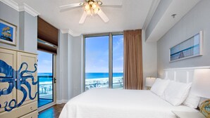 Habitación de hotel con una cama grande, ventilador de techo, vista a la playa y un armario con diseño azul.