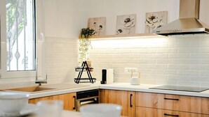 A modern kitchen with white brick backsplash, wooden cabinets, and a window with decorative ironwork. - Cretan Lodge Heated Pool (Agios Nikolaos)
