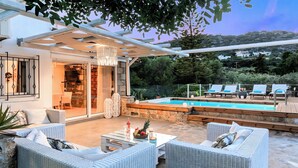 A covered outdoor area with a pool, wicker furniture, and a stone wall. - Cretan Lodge Heated Pool (Agios Nikolaos)