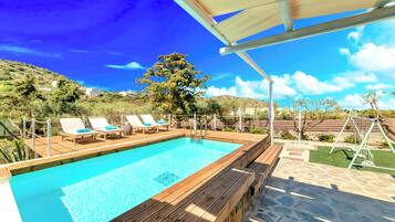 Una terraza de madera con piscina, sillas de descanso y un conjunto de columpios.