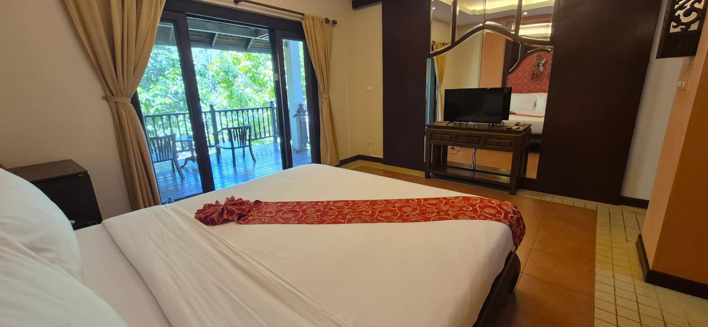 A hotel room with a large bed, a television on a wooden stand, and a balcony with a chair.