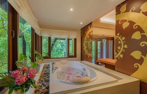 Ein Spa-Raum mit einer großen Badewanne, einer Holzbank und Blick auf üppiges Grün durch große Fenster.
