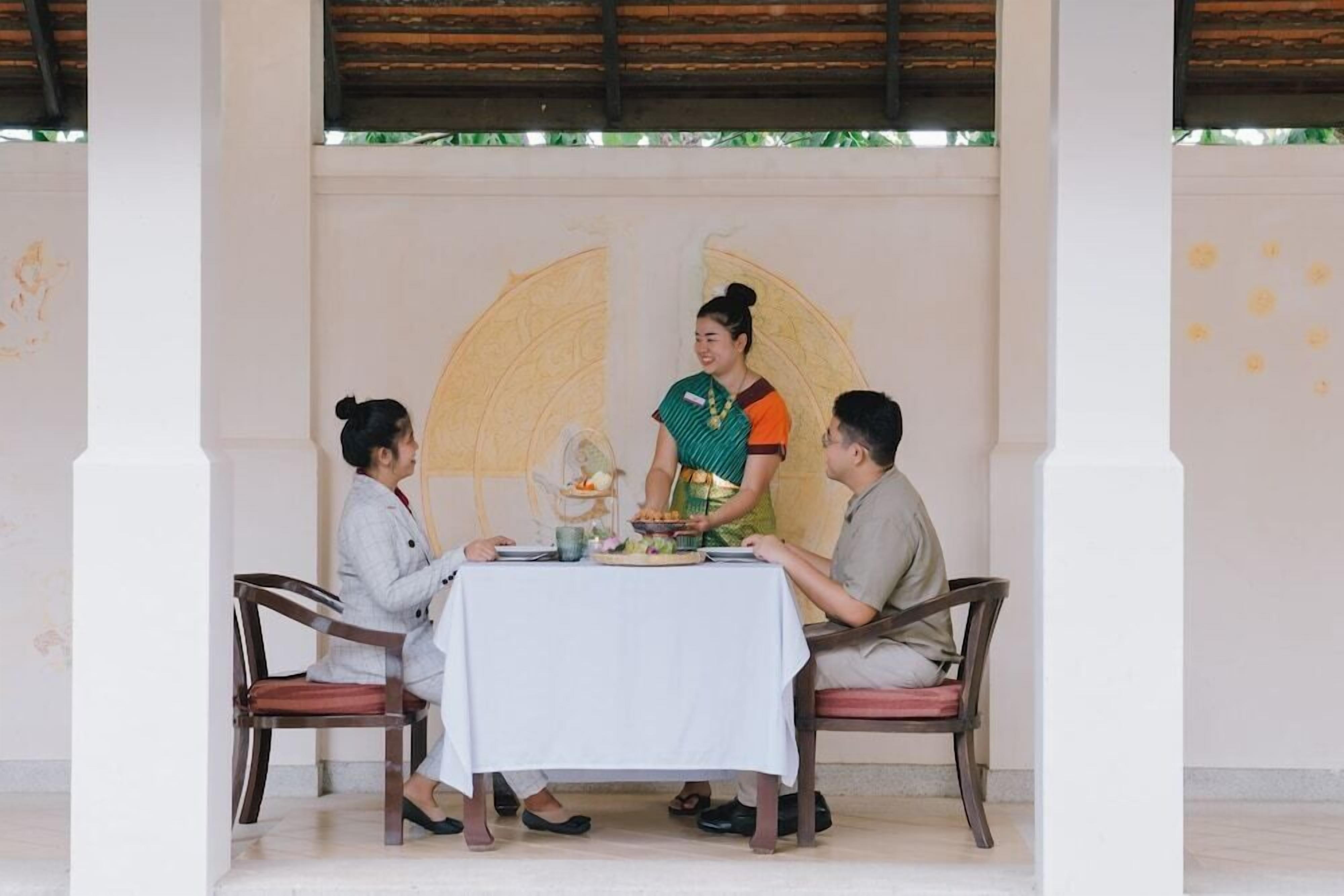 Un comedor con una mesa dispuesta para tres personas, un muro decorativo y un techo con vigas de madera.