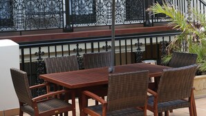 An outdoor patio with a wooden table and wicker chairs, a large umbrella, and a balcony with wrought iron railings. - Randwick Lodge (Sydney)