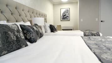 A hotel room with a tufted headboard, a large bed with white bedding, multiple pillows with floral patterns, a bedside table with a lamp, and a framed picture on the wall.