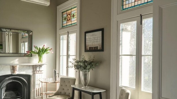 A room with a fireplace, two armchairs, a small table, and a vase with flowers. - Randwick Lodge (Sydney)