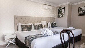 A hotel room with two beds, a white nightstand, a chair, and a wall-mounted air conditioner. - Randwick Lodge (Sydney)