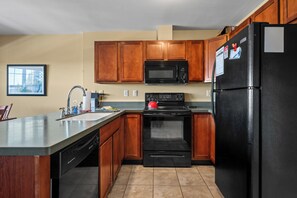 A kitchen with wooden cabinets, a black refrigerator, a microwave, and a stove.