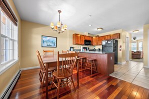 A modern kitchen with wooden cabinets, a central island with stools, and a dining area with chairs.