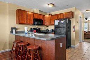 A kitchen with wooden cabinets, a black refrigerator, a microwave, a sink, and two stools.