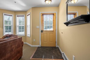 A hallway with a brown door, a brown couch, and a window with blinds.