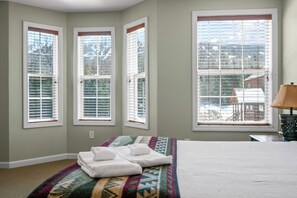 A bedroom with a bed, a colorful rug, and three windows with blinds. - Mountain Brook Condo 150 - Ski in ski out condo at Saddleback (Sandy River Plantation)