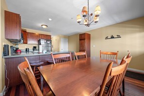 A dining area with a wooden table and chairs, a kitchen with wooden cabinets, and a chandelier.