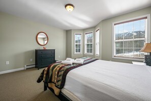 Een slaapkamer met een bed, een dressoir, een spiegel en ramen.