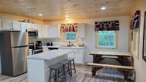 Una cocina moderna con armarios blancos, electrodomésticos de acero inoxidable, encimera de mármol y una mesa de madera con taburetes.