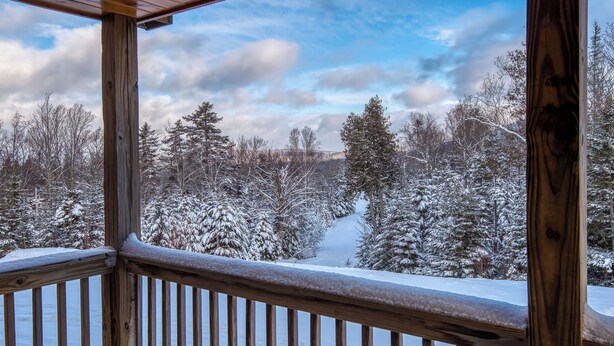A wooden deck with a view of snow-covered trees and a clear sky.