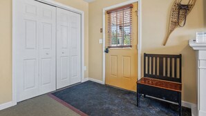 Un couloir avec une porte à deux battants, une fenêtre avec des stores, un banc et un objet fixé au mur.