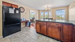 Une cuisine avec un réfrigérateur noir, des meubles de rangement en bois, une table à manger et un lustre.