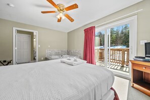 Un dormitorio con una cama grande, ventilador de techo, baño con bañera y puerta corrediza de vidrio que da a una terraza.