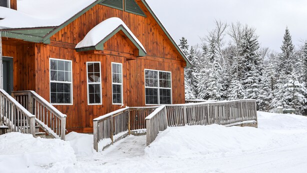 Une cabane en bois avec un escalier en bois menant à un porche, le tout entouré d’arbres couverts de neige.