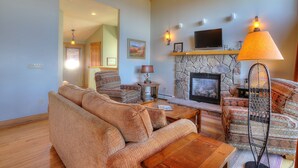 A cozy living room with a stone fireplace, a television mounted above it, and a comfortable seating area with a patterned sofa and armchairs.