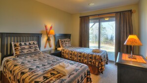 A hotel room with two beds, a window with curtains, a lamp, and a view of the outdoors.