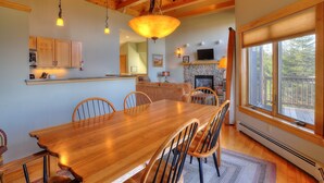 A spacious dining area with a wooden table and chairs, a stone fireplace, and a large window offering a view of the outdoors.
