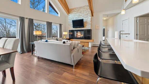 A modern living room with a fireplace, a flat-screen TV, and a dining area with bar stools. - Magalloway Loop Home 27 - Large family home at Saddleback (Rangeley)