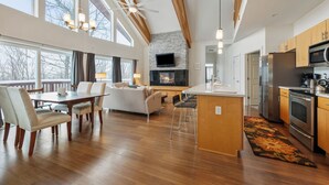 A spacious living area with a wooden ceiling, a fireplace, a TV mounted above it, and a kitchen with modern appliances. - Magalloway Loop Home 27 - Large family home at Saddleback (Rangeley)
