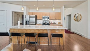 A modern kitchen with a central island, bar stools, stainless steel appliances, and a wooden upper level. - Magalloway Loop Home 27 - Large family home at Saddleback (Rangeley)