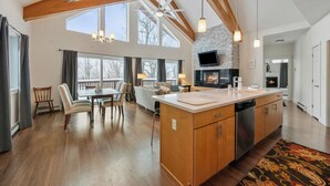 A spacious kitchen with a large island, wooden beams, and a stone accent wall. - Magalloway Loop Home 27 - Large family home at Saddleback (Rangeley)